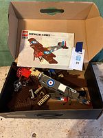 Original LEGO set 3451 Sopwith Camel pieces with instruction manual stored in a box, showing wing pieces, fuselage, and decals.
