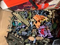 Large box filled with assorted loose vintage plastic toy soldiers in various colors and poses, including cavalry and infantry figures, with some bases and weapons visible.