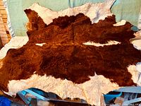 Full view of a large irregularly shaped cowhide rug with dark brown center and white borders, placed on a rustic table indoors.
