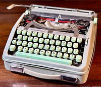 Front angled view of Hermes Baby typewriter showing mint green keys and metal body with handle attached to front.