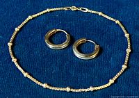 Sterling silver bracelet with intermittent small balls and wide hoop earrings displayed on dark blue fabric.