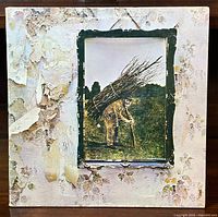 Front of Led Zeppelin IV album cover with peeling and wear on the sleeve showing a man carrying sticks in the framed photo.
