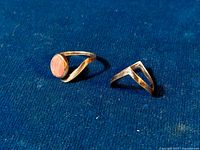 Two vintage sterling silver rings on blue cloth, one with a pink stone and one chevron shaped.