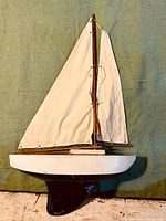 Full view of the vintage wooden sailboat model with cream canvas sails against a green background.