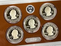 Obverse side of five 2015 U.S. quarters in protective plastic capsules within a brown display case.