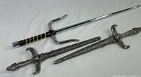 Photo showing one Japanese Oni Ninja octagon sai and two small Egyptian Pharaoh decorative daggers with silver-colored hilts and scabbards with hieroglyphic engravings.