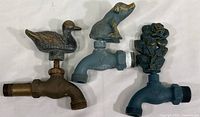 Overall top view of the three garden faucets showcasing the duck, pig, and rose bush decorative handles attached to the faucet bodies.