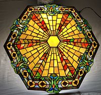 Top-down view of the stained glass lamp shade showing the full hexagonal pattern with yellow, orange, red, green, blue, and brown glass pieces forming a sunburst and floral motif.