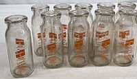 Group of 10 vintage clear glass milk bottles with orange Cloverleaf Farms logo