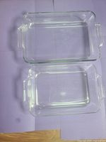 Two clear rectangular glass baking pans stacked, visible embossed measurement indicators on bottom surface and side handles.