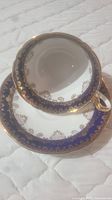 Photo of tea cup placed on the saucer showing the geometric blue and gold design and gold trim.