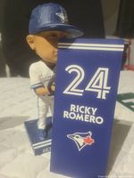 Front and side view of Ricky Romero bobblehead holding a baseball glove, with backdrop panel showing number 24, name and Blue Jays logo.