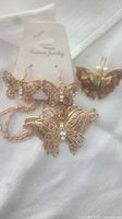 Set of gold-tone butterfly brooch, earrings on card, chain with butterfly pendant on white fabric background