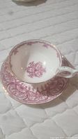 Photo of white bone china teacup decorated with detailed pink floral and scroll patterns and gold trim