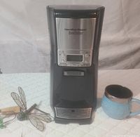 Front view of Hamilton Beach BrewStation coffee maker with a blue ceramic mug and decorative dragonfly on left