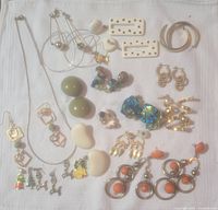 Full view of various pairs of costume earrings laid out on white cloth showing a variety of styles including hoops, clip-ons, studs, and dangly earrings in multiple colors and materials.