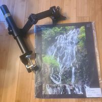 Desk monitor pole stand and wrapped waterfall poster shown on wooden floor.