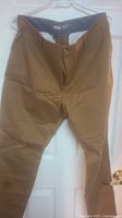 Front view of light brown men's pants hanging on a hanger.