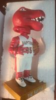 Close-up of The Raptor bobblehead in original foam packaging, showing red dinosaur figure in Toronto Raptors uniform number 95, holding basketball, on gold base.