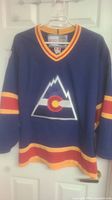Front view of dark blue hockey jersey with red and yellow stripes, large Colorado Avalanche logo on front.