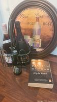Photo showing the book 'Night Road' by Kristin Hannah, Freixenet Cordon Negro sparkling wine, Stone's Original London Dry Ginger Beer bottle, a small jar, and a round wooden tray with wine-themed graphics.
