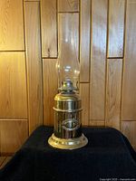 Brass oil lamp with tall clear glass chimney, metallic brass body, and circular base