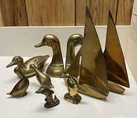 Assortment of brass decorative figures including 3 duck figures, 1 pair of duck head bookends, 2 sailboats, 1 penguin, 1 dolphin
