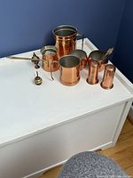 Photo of 6 assorted copper items arranged on white surface: 1-liter mug, small mugs, cezve, and salt & pepper shakers