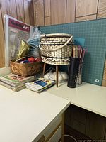 Collection of various craft items including knitting needles, patterns, basket, and threads on a table.