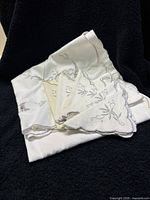 White fabric napkins with light floral embroidery laid on black background