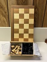 Closed wooden chess board with compartments holding light and dark wooden chess pieces, showing condition and pieces included.