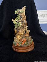 Front view of the chipmunk sculpture showing the two chipmunks, green bird, oak leaves, acorns, and the wooden base.