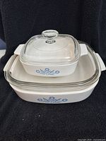 Stacked view of two Corning Ware baking dishes with lids showing blue floral pattern on white base.