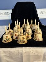 Full view of all 15 porcelain bells with hand-painted Hummel figures, arranged in three rows on black felt.