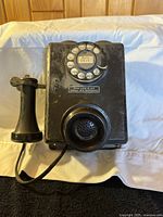 Front view of historic black wall telephone with rotary dial and attached handset.