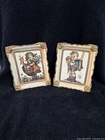 Two wood framed Hummel pictures featuring School Boy and Village Girl characters on black backdrop.