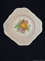 Fruit plate with orange and berries illustration on pale pink background, showing scalloped textured edge.