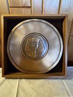 Full view of the bronze plate with King Tutankhamun mask centered in a wooden frame.