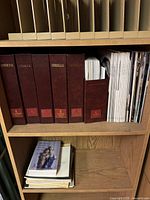 Shelf with four large burgundy LLADRO Collectors Society binders, a box file filled with magazines, and a small stack of books and papers beneath.