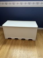 Front view of the white painted wooden storage bench, closed lid, showing scalloped cutouts at the base for ventilation.