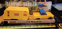 Side view of yellow truck and camper trailer in original packaging, with a measuring tape for size reference.