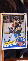 Front photo of 1984-85 Doug Gilmour rookie hockey card, showing player in Blues uniform skating on ice and inset portrait in bottom right corner