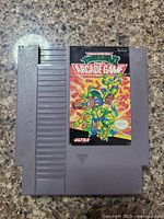 Photo of the front of the gray NES cartridge featuring the colorful game label with Teenage Mutant Ninja Turtles illustration and title.