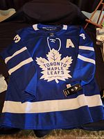 Front view of new blue and white Toronto Maple Leafs jersey with Auston Matthews logo and number, Adidas tags attached.