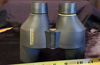 Side view of Bushnell binoculars showing brand name and size approximation using a ruler.