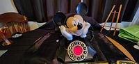 Front angled view of the black rotary dial Mickey Mouse phone with the character facial expression visible.
