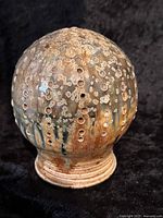 Full view of the pierced globe pottery sculpture showing texture, shape and glaze colors.