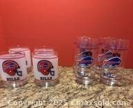 Two sets of Buffalo Bills collectors glasses: 4 short glasses with helmet logo and 4 taller glasses with buffalo logo, displayed on counter against red background.