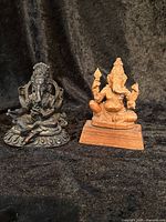 Both Ganesh statues together, one dark metal and one carved mahogany on a wooden base.
