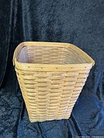 Front angled view of woven natural wood Longaberger medium waste basket with plastic liner inside.